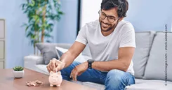 Wie ist die Funktionsweise von Prämiensparen? Das Bild zeigt einen Mann der Geld in sein Sparschwein einzahlt, um es später für das Prämiensparen zu nutzen